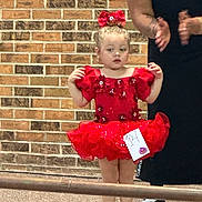 bow, brick_wall, celebration, child, clapping, costume, cute, dance, dress_up, event, floor, girl, indoor, number_tag, person, red_dress, toddler, tutu, white_shoes, young_child