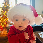 Justus is registered to the contest to win money with this photo: baby, child, santa_hat, christmas, holiday, festive, red_clothing, indoor, portrait, cute, wide_eyes, hand, face, soft_light, decorations, tree, blurred_background, warm, cozy, celebration