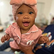 Syanne is registered to the contest to win money with this photo: baby, child, pink_hat, pajamas, smiling, happy, indoor, person, hands, closeup, cute, infant, portrait, soft_texture, warm_colors, blurred_background, human, face, headwear, apparel