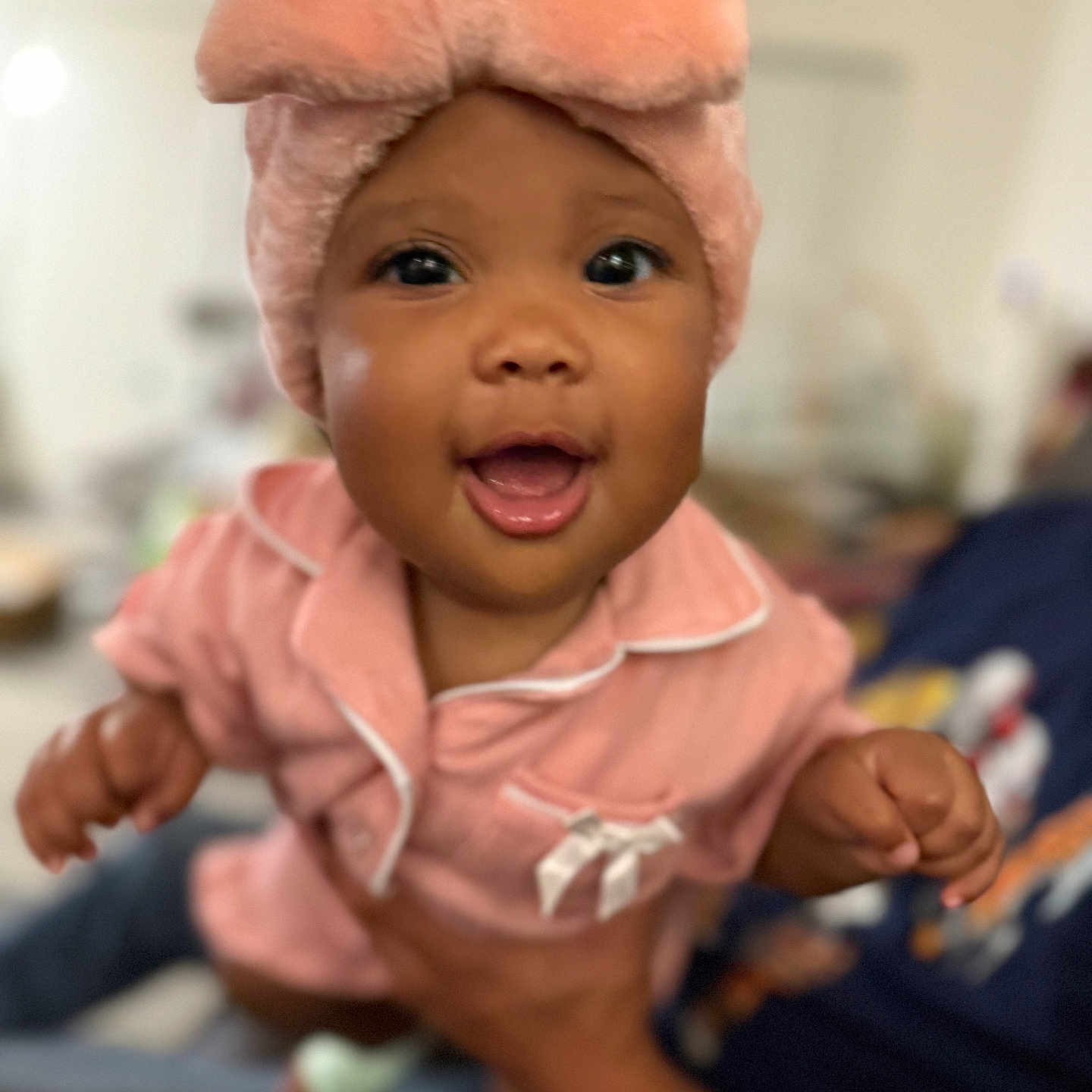 Syanne is registered to the contest to win money with this photo: apparel, baby, blurred_background, child, closeup, cute, face, hands, happy, headwear, human, indoor, infant, pajamas, person, pink_hat, portrait, smiling, soft_texture, warm_colors