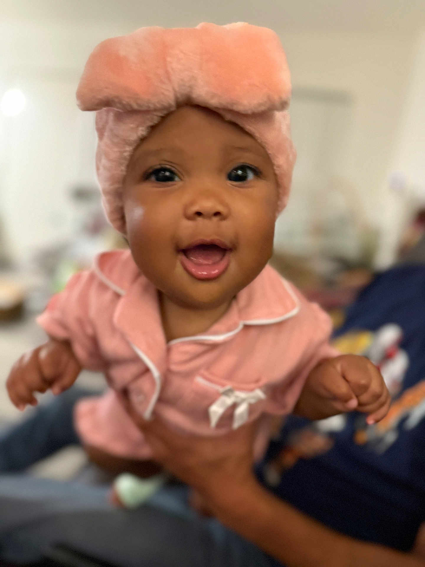 Syanne is registered to the contest to win money with this photo: baby, child, pink_hat, pajamas, smiling, happy, indoor, person, hands, closeup, cute, infant, portrait, soft_texture, warm_colors, blurred_background, human, face, headwear, apparel
