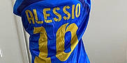 Alessio a rejoint le concours — aidez-le/la à gagner de superbes lots ! child, back_view, blue_jersey, sportswear, number_10, name_print, indoor, door, tiled_floor, short_hair, casual_clothing, pants, standing, young_boy, bright_colors, fabric, clothing, person, hair, childhood
