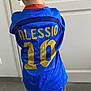 child, back_view, blue_jersey, sportswear, number_10, name_print, indoor, door, tiled_floor, short_hair, casual_clothing, pants, standing, young_boy, bright_colors, fabric, clothing, person, hair, childhood