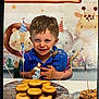 child, boy, birthday, cake, candle, donuts, cookies, party, celebration, smiling, happy, blue_shirt, table, sparkler, animal_backdrop, giraffe, elephant, lion, indoor, food