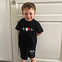 Alessio a rejoint le concours — aidez-le/la à gagner de superbes lots ! child, boy, smile, curly_hair, black_shirt, black_shorts, italia, indoor, door, white_door, standing, socks, floor, tile_floor, happy, person, casual_clothing, young_child, portrait, cute