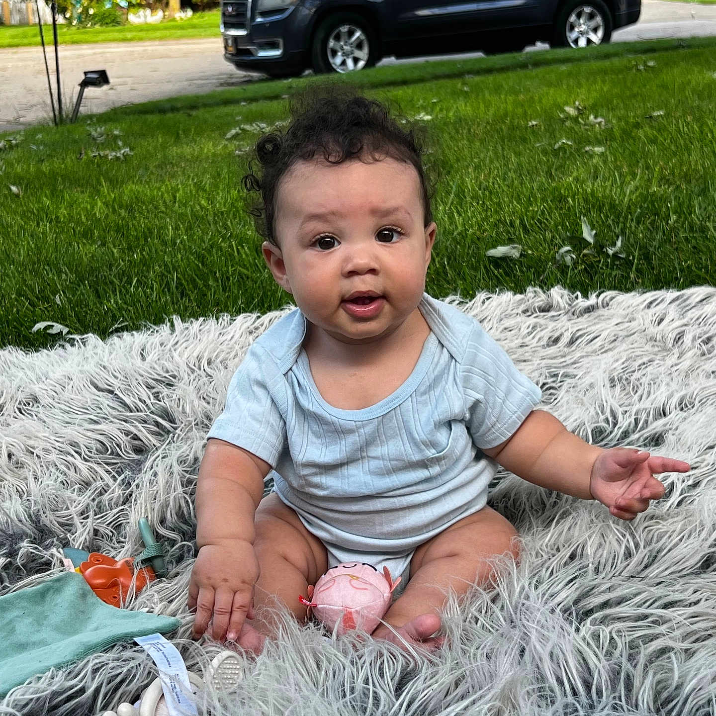 Khyson joined the competition — help win amazing prizes! baby, blanket, blue_onesie, child, curly_hair, cute, daylight, face, foot, grass, hand, infant, lawn, outdoor, parked_car, person, residential_area, sitting, skin, toy