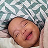 baby, bed, bedding, blanket, close_up, cozy, eyes_closed, face, geometric_pattern, hand, happy, home, indoors, infant, mouth_open, peaceful, pink_blanket, portrait, sleeping, smiling