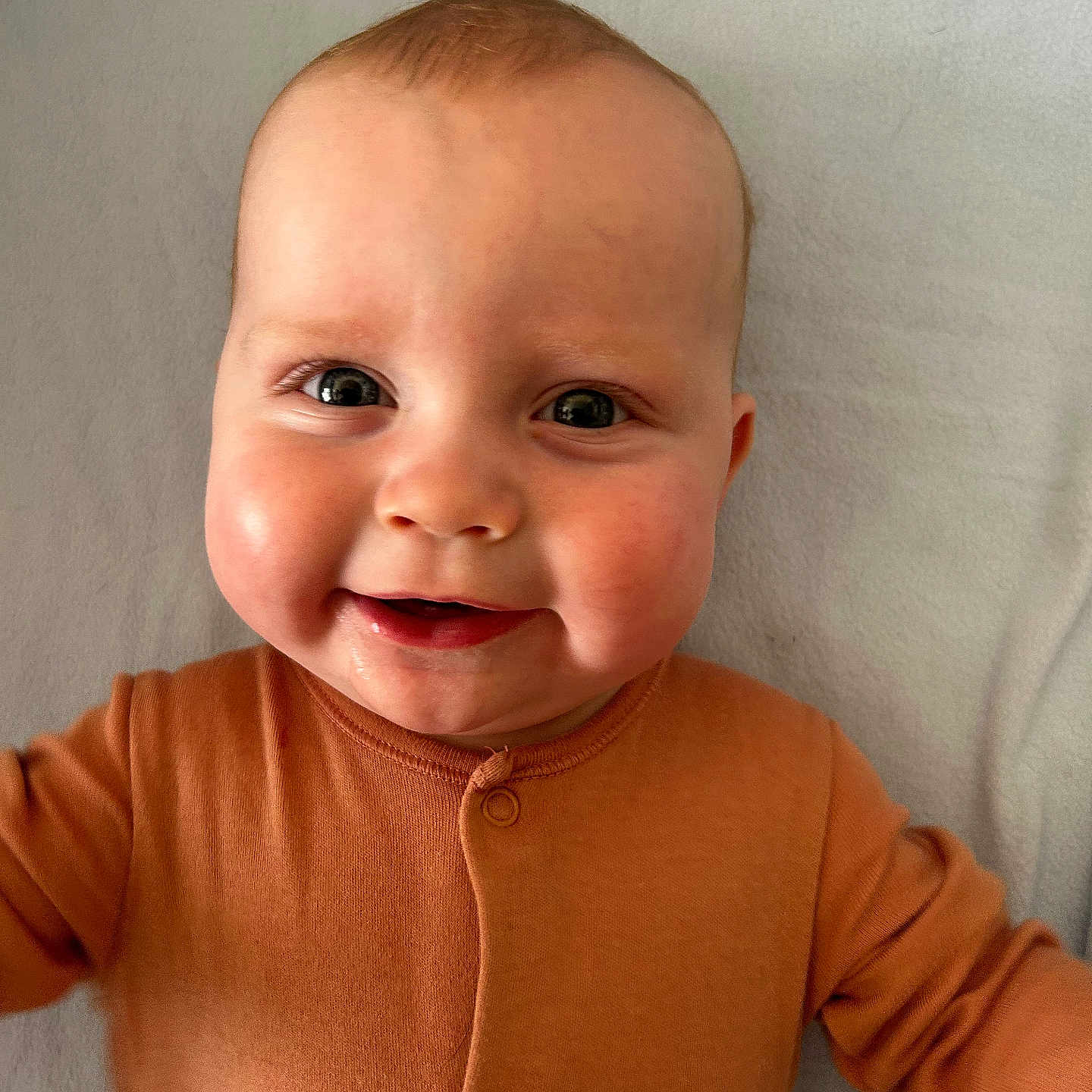 Harry joined the competition — help win amazing prizes! baby, blanket, buttoned_outfit, cheeks, child, closeup, cute, eyes, face, happy, head, indoors, infant, lying_down, orange_clothing, portrait, skin, smiling, soft_texture, young_child