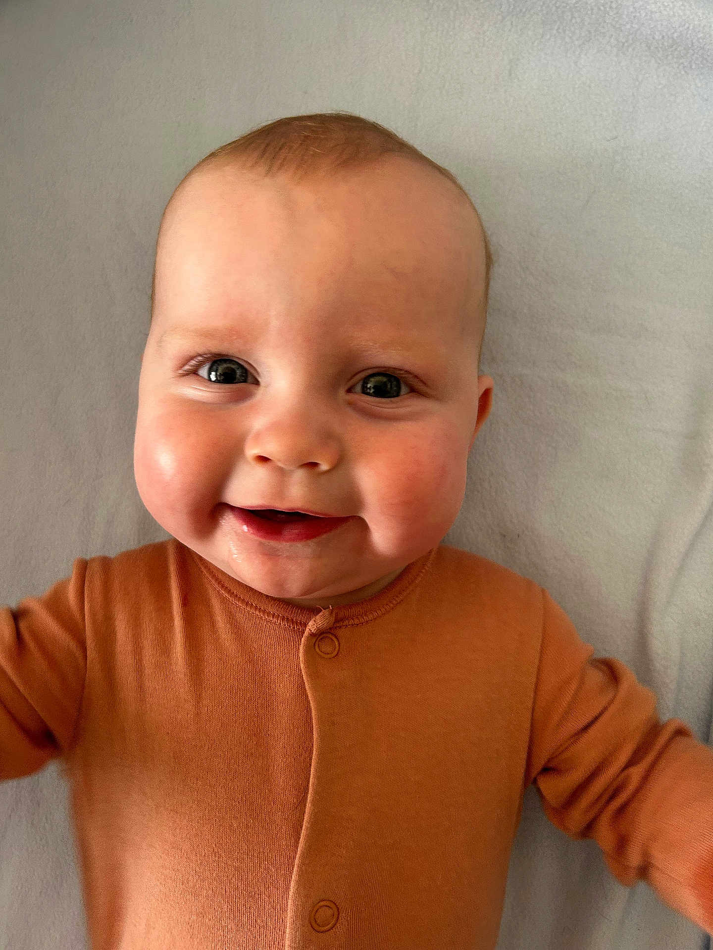 Harry joined the competition — help win amazing prizes! baby, child, smiling, face, cheeks, orange_clothing, infant, lying_down, closeup, happy, cute, skin, eyes, buttoned_outfit, indoors, portrait, young_child, head, soft_texture, blanket