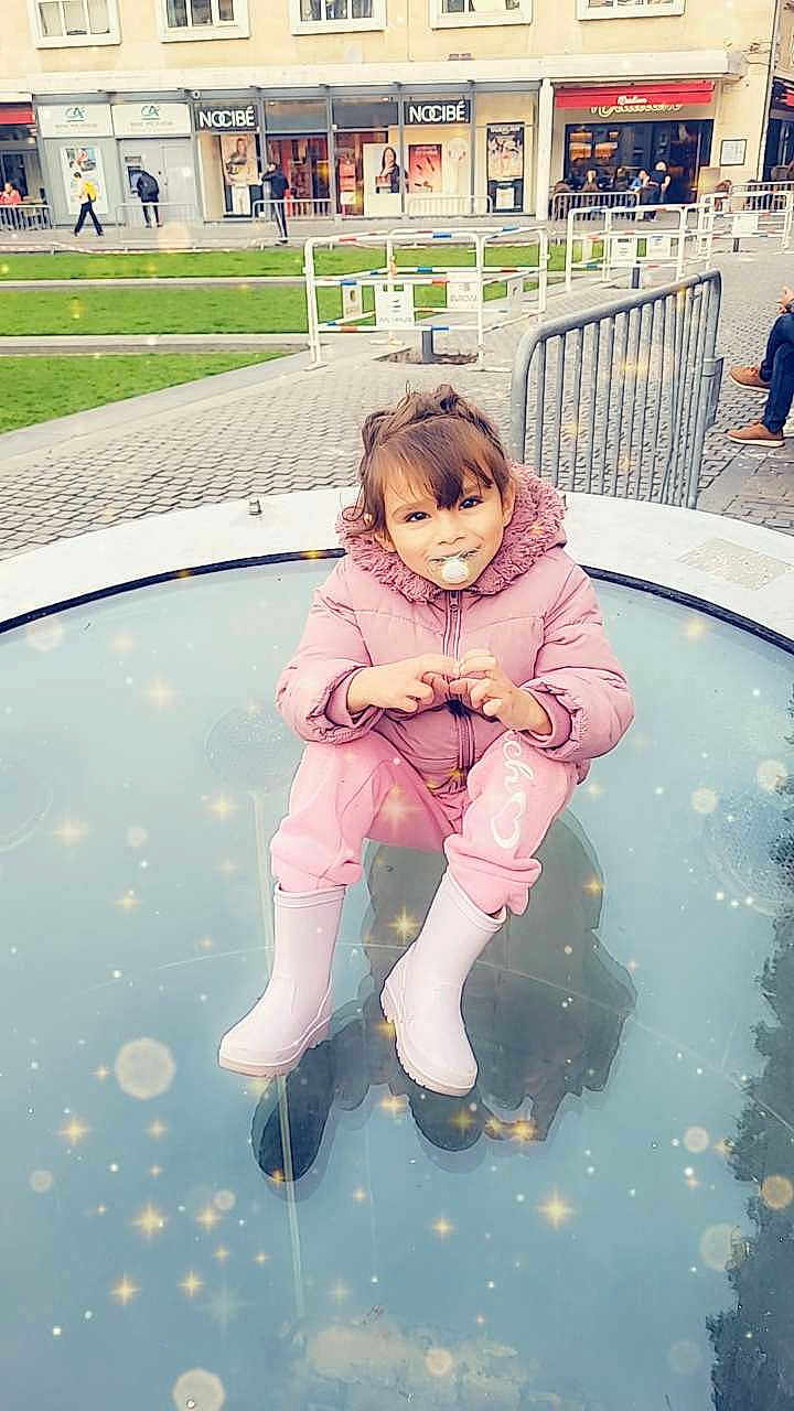Illanna a rejoint le concours — aidez-le/la à gagner de superbes lots ! building, casual, child, cute, daylight, fence, glass_surface, outdoor, pacifier, people, pink_jacket, playful, posing, rain_boots, reflection, sparkles, street, toddler, urban, winter_clothing