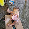 baby, child, cardboard_box, carpet, living_room, leather_chair, yellow_pillow, smiling, waving_arms, person, indoors, foot, pink_clothing, happy, playful, home, cute, toddler, package, box