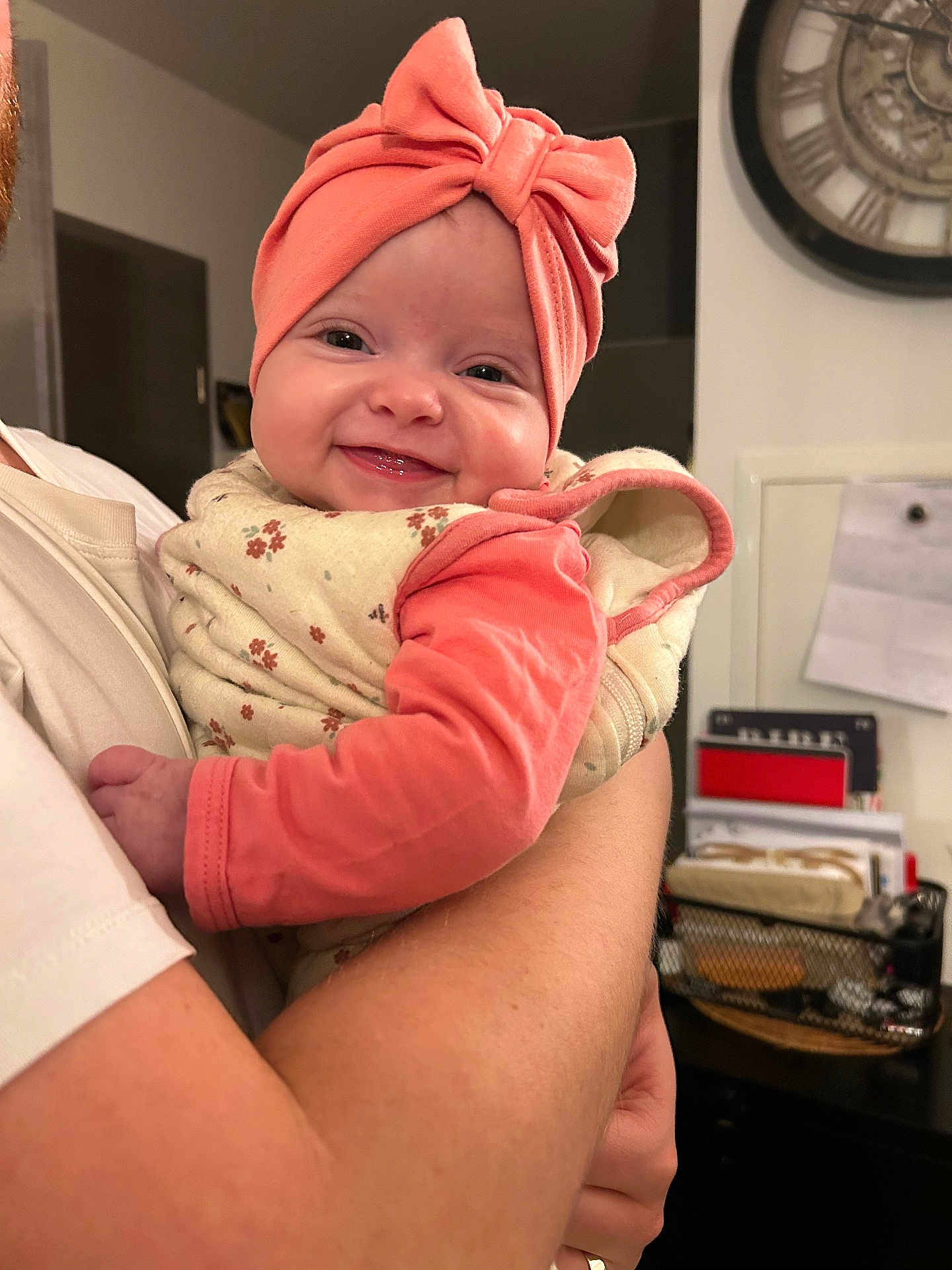 Mira a rejoint le concours — aidez-le/la à gagner de superbes lots ! baby, smile, headband, bow, infant, person, arm, clothing, floral_pattern, indoor, holding, adult, face, cute, happy, portrait, human, baby_girl, closeup, warm_lighting