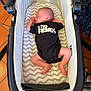 baby, newborn, sleeping, bassinet, onesie, clothing, chevron_pattern, mattress, indoor, floor_tiles, terracotta, furniture, wicker, feet, hands, head, person, infant, cozy, resting