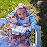 baby, infant, child, outdoor, grass, stroller, seat, portrait, smiling, face, pink_hat, bow, clothing, stuffed_animal, giraffe_toy, bunny_toy, baby_toys, blanket, sunlight, playtime