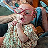 baby, infant, child, portrait, glasses, pink_glasses, floral_dress, dress, surprised, open_mouth, sitting, being_held, indoor, home, adult, arms, baby_swing, furniture, cozy, close_up