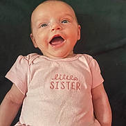 Harper is registered to the contest to win money with this photo: baby, infant, pink_clothing, smiling, happy, face, child, cute, portrait, baby_girl, sleeveless_dress, text_on_clothing, lying_down, human, skin, head, eyes, mouth_open, cheeks, newborn