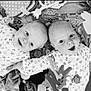 baby, infant, smiling, lying_down, toys, blanket, patterned_clothing, cute, playful, face, child, black_and_white, happy, indoors, two_babies, closeup, expression, young, adorable, peaceful