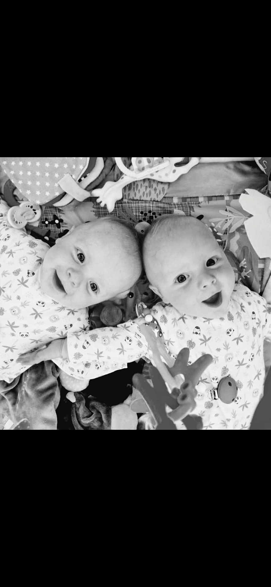 Elio Et Noa participe au concours pour gagner de l'argent avec cette photo : baby, infant, smiling, lying_down, toys, blanket, patterned_clothing, cute, playful, face, child, black_and_white, happy, indoors, two_babies, closeup, expression, young, adorable, peaceful