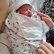 Amari is registered to the contest to win money with this photo: newborn, baby, blanket, swaddled, sleeping, hat, hand, floral_pattern, bed, soft_texture, cozy, person, infant, resting, cute, skin, wrapped, tenderness, family, comfort
