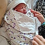 newborn, baby, blanket, swaddled, sleeping, hat, hand, floral_pattern, bed, soft_texture, cozy, person, infant, resting, cute, skin, wrapped, tenderness, family, comfort