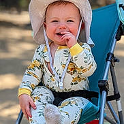 Olivia is registered to the contest to win money with this photo: baby, child, smiling, hat, stroller, outdoor, pajamas, floral_pattern, hand, footwear, seat, happy, face, infant, sunhat, cute, portrait, playful, person, daylight