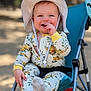 baby, child, smiling, hat, stroller, outdoor, pajamas, floral_pattern, hand, footwear, seat, happy, face, infant, sunhat, cute, portrait, playful, person, daylight