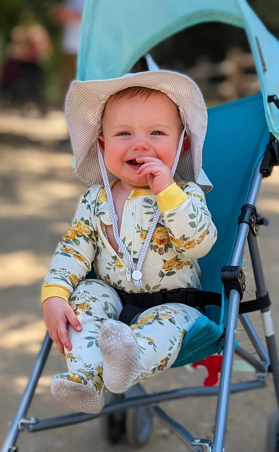 Olivia is registered to the contest to win money with this photo: baby, child, smiling, hat, stroller, outdoor, pajamas, floral_pattern, hand, footwear, seat, happy, face, infant, sunhat, cute, portrait, playful, person, daylight