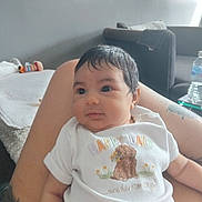 A'Va joined the competition — help win amazing prizes! baby, infant, person, child, legs, tattoo, white_onesie, dog_print, text_on_clothing, living_room, couch, blanket, toy, water_bottle, arm, hair, face, eyes, skin, comfort