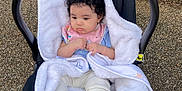 A'Va is registered to the contest to win money with this photo: baby, baby_carrier, black_carrier, blanket, child, clothing, curly_hair, cute, gravel, greenery, infant, nature, outdoor, pink_bib, plants, portrait, seated, small, socks, white_blanket
