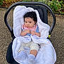 baby, baby_carrier, black_carrier, blanket, child, clothing, curly_hair, cute, gravel, greenery, infant, nature, outdoor, pink_bib, plants, portrait, seated, small, socks, white_blanket