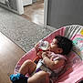 baby, bottle, toy, indoor, carpet, floor, baby_bouncer, pink, milk, child, curly_hair, clothing, socks, toy_in_hand, seat, kitchen, doorway, flooring, person, relaxing