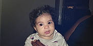 A'Va joined the competition — help win amazing prizes! baby, child, curly_hair, onesie, hand, adult, indoor, person, sitting, cute, infant, holding, dark_skin, expression, portrait, looking, eyes, small, room, door