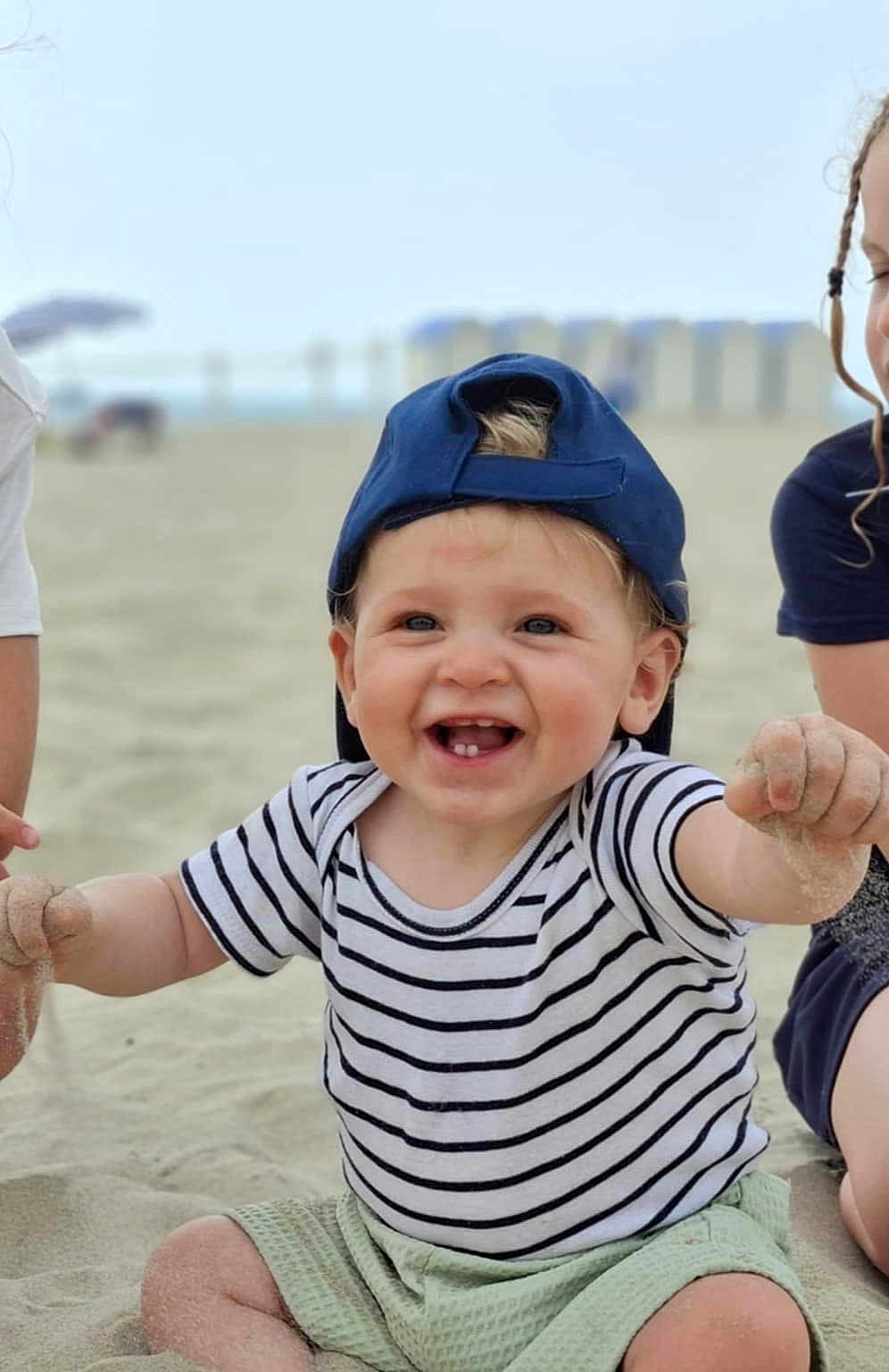 Naé a rejoint le concours — aidez-le/la à gagner de superbes lots ! toddler, child, beach, sand, smiling, cap, striped_shirt, happy, outdoor, play, summer, cute, baby, person, casual_clothing, fun, sunny, daytime, sitting, joy