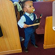 Dru joined the competition — help win amazing prizes! toddler, child, pacifier, blue_suit, bow_tie, black_shoes, church, pew, carpet, wooden_pew, person, indoor, holding_object, standing, curious, people_in_background, formal_wear, young_child, hat, stick