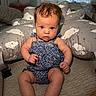 baby, child, infant, blue_eyes, curly_hair, romper, cushion, cloud_pattern, indoor, soft_lighting, sitting, cute, curious, skin, person, furniture, room, floor, support, portrait