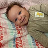 baby, smiling, blue_eyes, blanket, patterned_blanket, beige_outfit, winnie_the_pooh_patch, lying_down, cute, cozy, happy, infant, child, soft_texture, curly_hair, indoor, portrait, closeup, warm, adorable