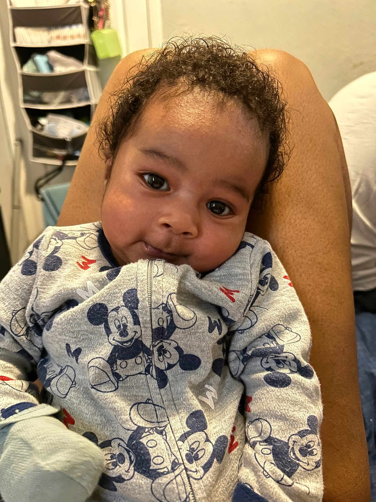 Jackson is registered to the contest to win money with this photo: baby, child, curly_hair, mickey_mouse, clothing, sleeper, infant, person, smiling, cute, indoor, lap, cozy, portrait, face, young_child, soft_lighting, casual, home, comfortable
