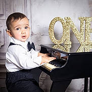 Luar joined the competition — help win amazing prizes! toddler, child, piano, miniature_piano, bow_tie, white_shirt, black_pants, celebration, birthday, number_one, gold_glitter, music, indoors, portrait, young_child, hands_on_piano, expression, face, cute, formal_wear
