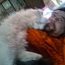 man, cat, indoor, orange_shirt, fluffy_cat, lying_down, cuddle, blurry, facial_hair, beanie, close_up, pet, furniture, relaxation, cozy, casual, home, companion, friendship, indoor_lighting