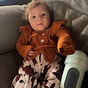 Emersyn joined the competition — help win amazing prizes! baby, infant, child, couch, clothing, patterned_pants, curly_hair, sippy_cup, indoor, face, person, relaxing, seated, cozy, soft_lighting, home, furniture, cute, looking_at_camera, casual