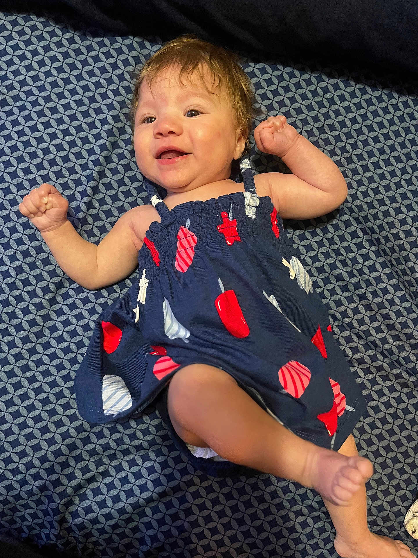 Emersyn is registered to the contest to win money with this photo: baby, child, smiling, dress, patterned_clothing, blue_blanket, happy, infant, arms_up, lying_down, cute, face, cheerful, indoors, skin, foot, hand, head, young_child, fabric