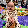 baby, child, leopard_print, plush_toy, giraffe, play_mat, indoor, people, smile, headband, pajamas, sitting, woman, man, group, floor, toy, colorful, happy, playtime
