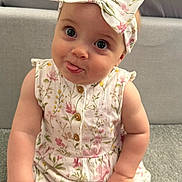 Olivia is registered to the contest to win money with this photo: baby, child, infant, bow, floral, dress, carpet, couch, cute, tongue_out, sitting, indoors, smiling, portrait, playful, headband, person, clothing, skin, furniture