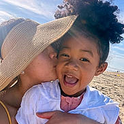 Kamilla is registered to the contest to win money with this photo: child, adult, beach, sunhat, kiss, smile, curly_hair, ocean, sky, sand, hug, happy, outdoor, sunlight, portrait, affection, family, vacation, casual_clothing, warm_weather