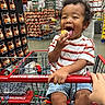 toddler, child, shopping_cart, costco, food, warehouse, shelves, snack, curly_hair, striped_shirt, happy, smiling, indoor, supermarket, retail, person, hand, clothing, blue_shorts, grocery