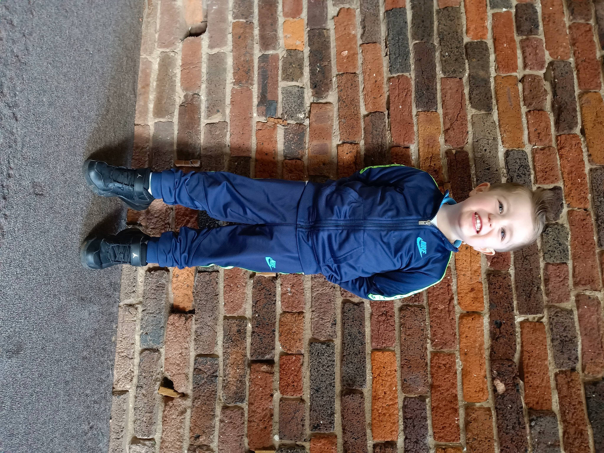 Armani is registered to the contest to win money with this photo: brick, brickwork, cobblestone, composite_material, denim, electric_blue, flooring, human, human_leg, joy, leg, line, pattern, person, road_surface, shadow, sidewalk, sitting, standing, textile