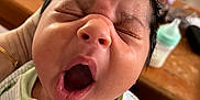 Kingsley is registered to the contest to win money with this photo: baby, newborn, yawning, close_up, face, hand, onesie, green, white, infant, sleepy, cute, mouth_open, eyes_closed, soft, indoor, blurred_background, flower, baby_bottle, person