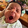 baby, newborn, yawning, close_up, face, hand, onesie, green, white, infant, sleepy, cute, mouth_open, eyes_closed, soft, indoor, blurred_background, flower, baby_bottle, person