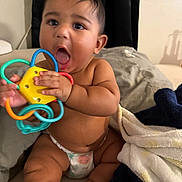 Kingsley joined the competition — help win amazing prizes! baby, child, toy, colorful, diaper, sitting, blanket, bed, indoor, cute, chubby, playful, expression, hand, footwear, sock, skin, face, mouth, curly_hair