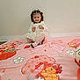 child, toddler, girl, blanket, pink, dress, smile, sitting, wall, floor, strawberry, cartoon, portrait, curly_hair, hair_bow, shoes, polka_dots, headband, happy, indoors